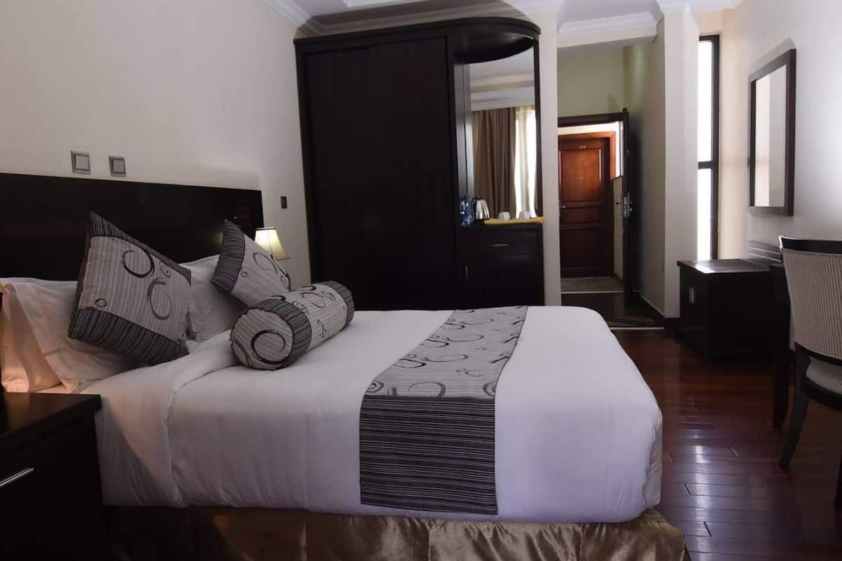 A hotel room with a large bed, a nightstand, a desk, and a chair.
