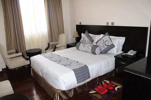 A hotel room with a large bed, a chair, a small table, a lamp, and a telephone on the nightstand.