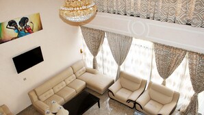 A living room with a sectional sofa, two armchairs, a coffee table, and a TV mounted on the wall. - Southern Addis Hotel (Addis Ababa)