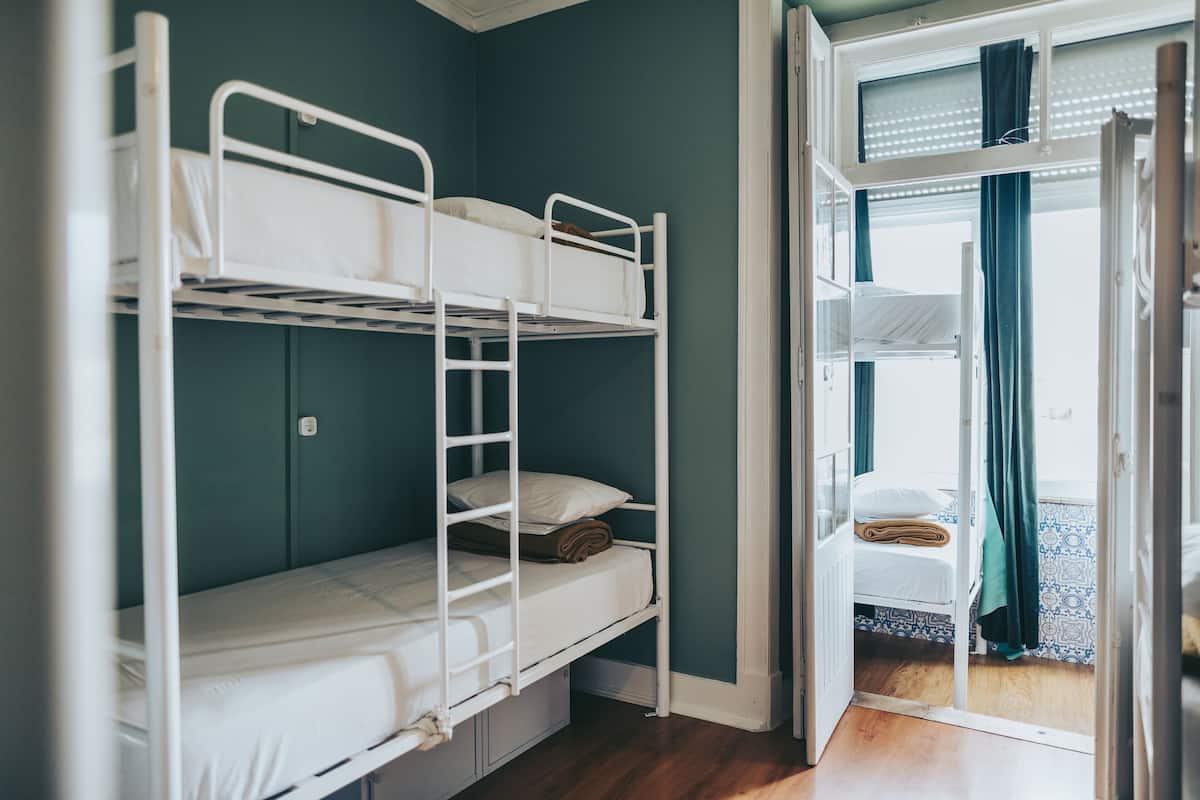 Un dormitorio con literas, una puerta que da a otra habitación y una ventana con cortinas.