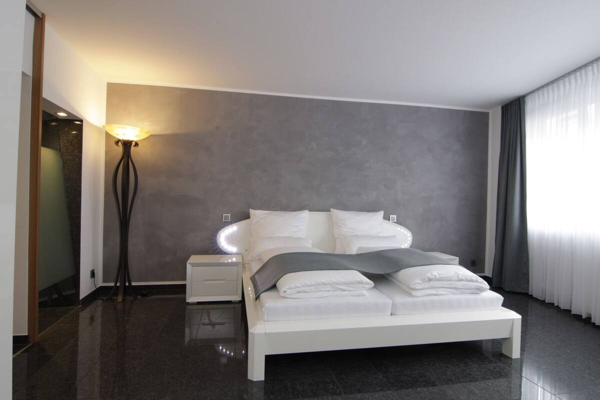 A modern bedroom with a bed, bedside tables, a floor lamp, and a large window with curtains.