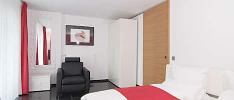 Una habitación de hotel moderna con una cama bien hecha, una silla negra, un armario de madera y un espejo grande en la pared.