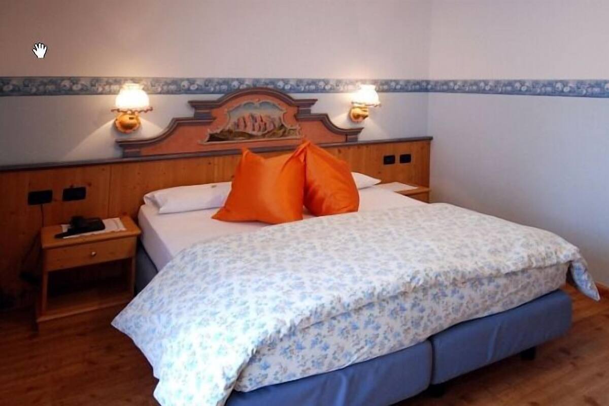 A bedroom with a bed, two nightstands, a headboard with a decorative panel, and two wall-mounted lamps.