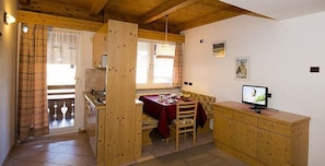 Une cuisine chaleureuse avec des meubles de rangement en bois, une table à manger recouverte d’une nappe rouge et un téléviseur posé sur un meuble en bois.