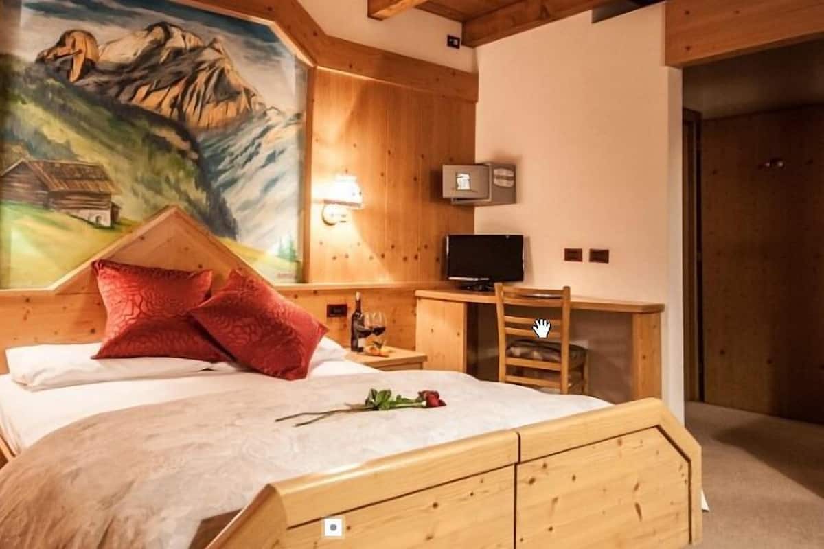 A wooden bedroom with a bed, two bedside tables, a TV, and a painting of mountains.