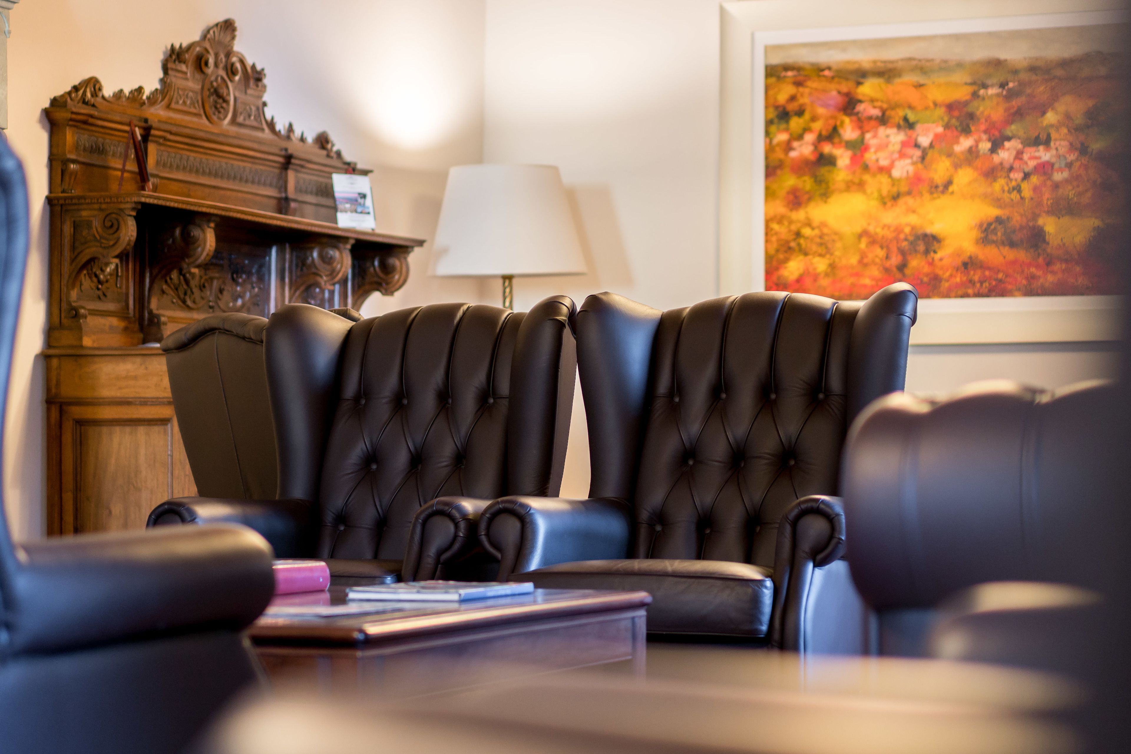 A room with two black leather armchairs, a wooden cabinet, and a painting on the wall.