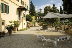 A courtyard with outdoor seating, potted plants, and a view of a castle in the distance.