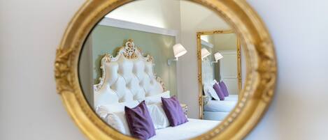 A bedroom with a large round mirror, a tufted headboard, and purple pillows.