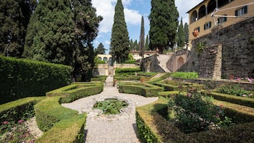A formal garden with geometric hedges, a central pond, and tall cypress trees.