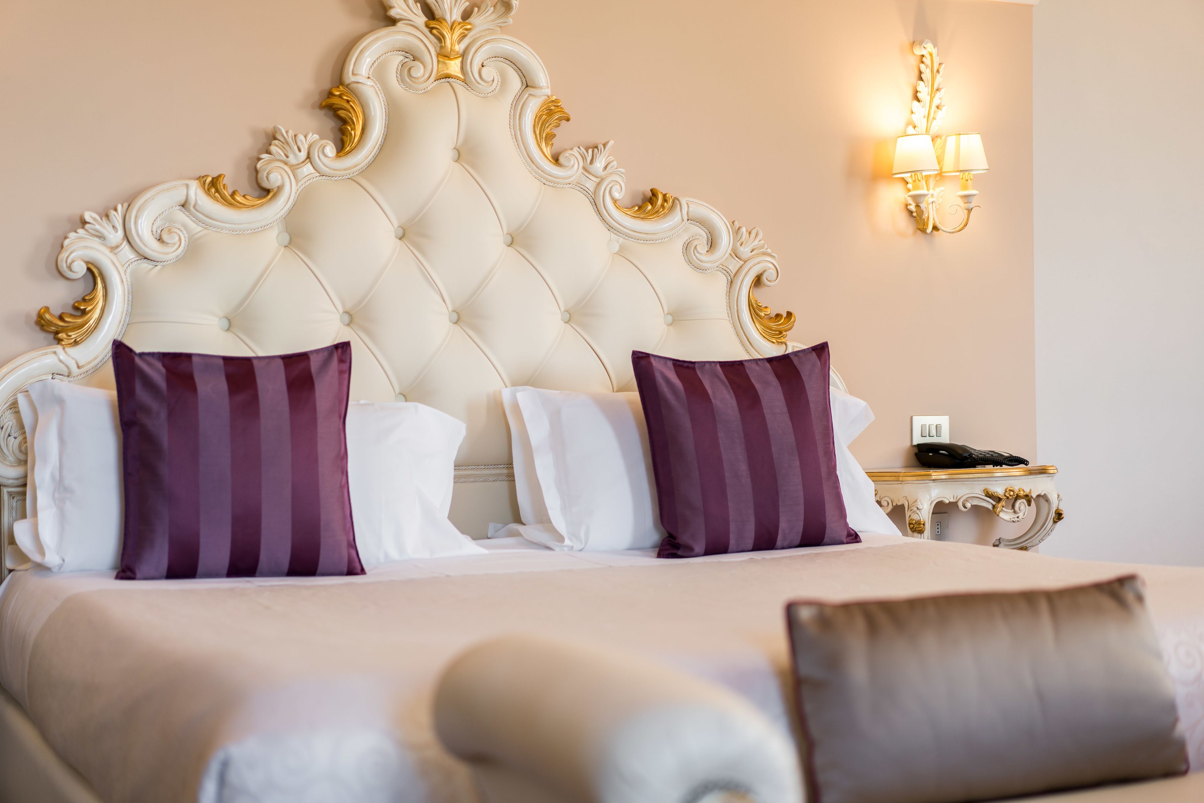 Una habitación de hotel con cabecera capitonada, dos almohadas, una mesita de noche con lámpara y teléfono.