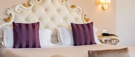 A hotel room with a tufted headboard, two pillows, a bedside table with a lamp, and a phone.