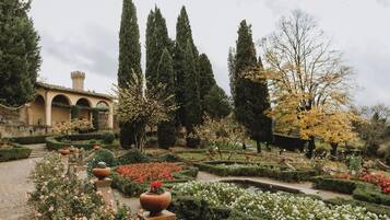 Ein formal gestalteter Garten mit Formschnitten, einer Fontäne und einem Gebäude mit einem Turm.