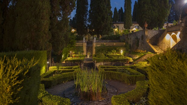 Un jardín formal con setos recortados, una fuente central y senderos de piedra.