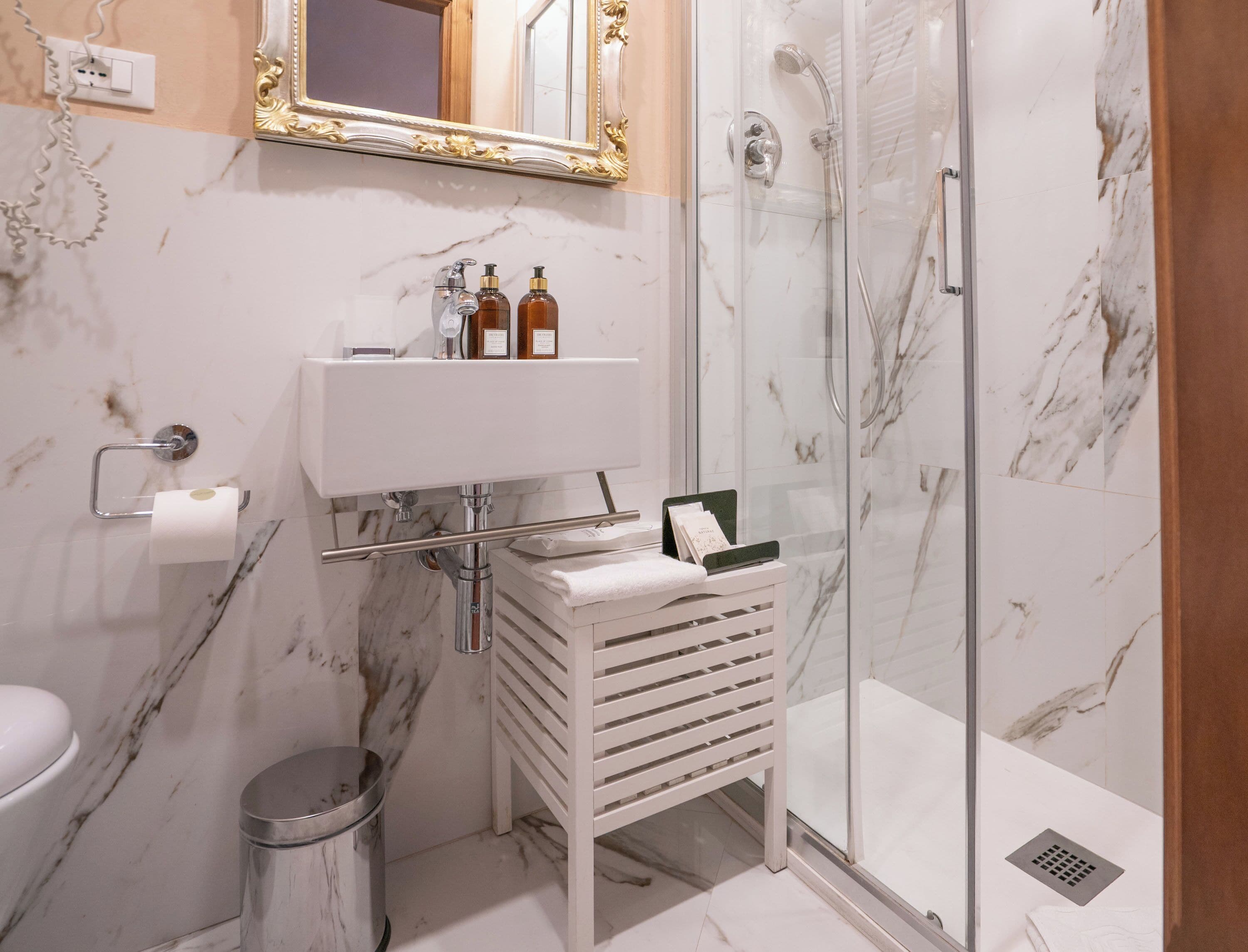 A bathroom with a marble sink, a glass shower enclosure, a toilet, and a trash can.