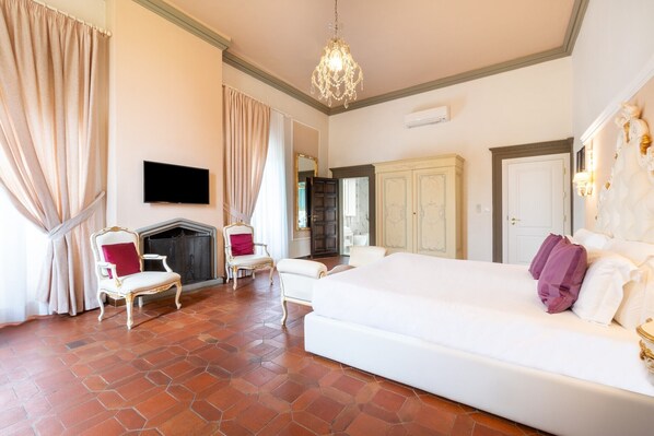 A bedroom with a large bed, a fireplace, two chairs, a television, and a wardrobe. - Art Hotel Villa Agape (Florence)
