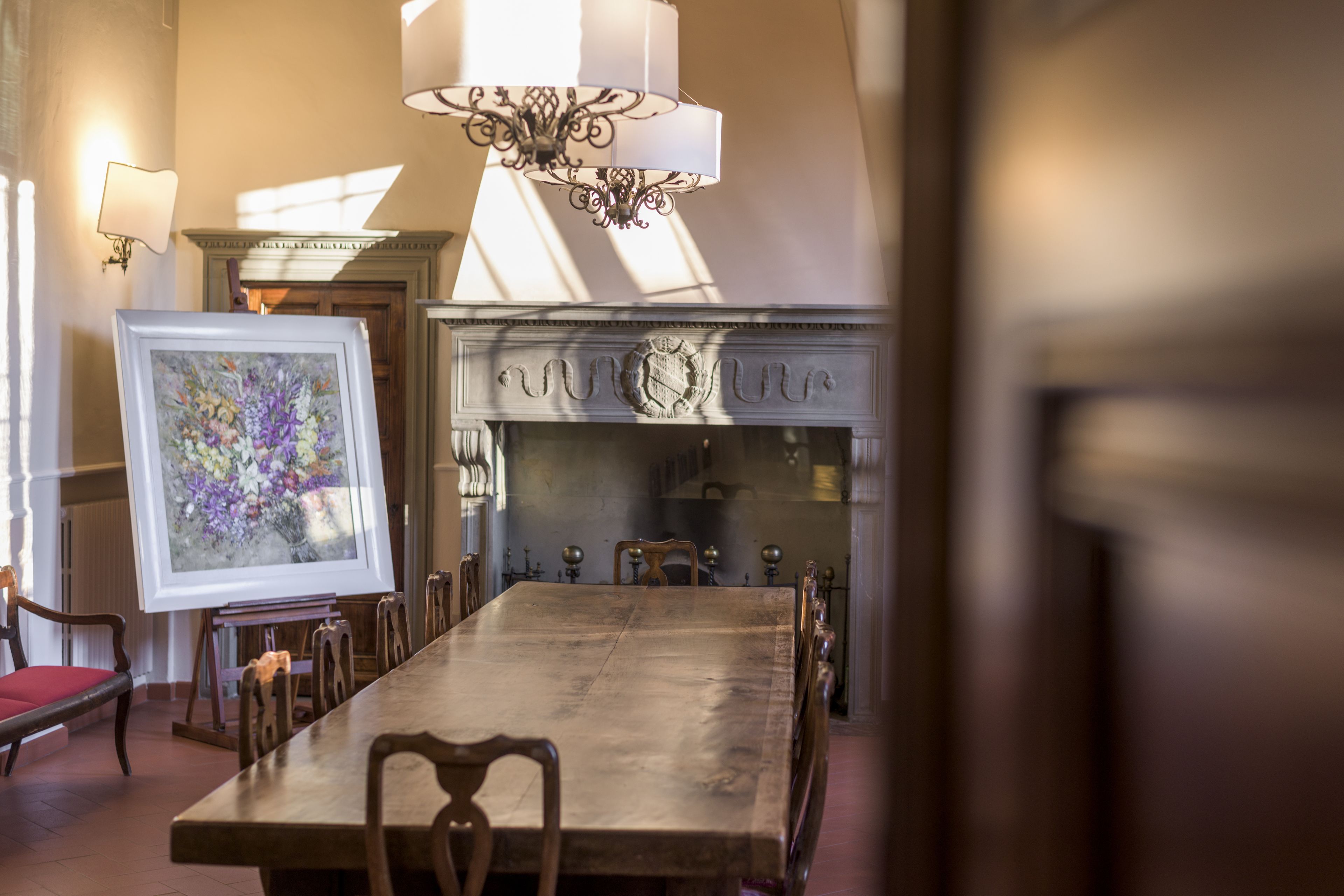 A dining room with a large wooden table, chairs, a chandelier, and a fireplace.