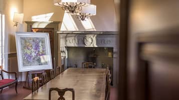 A dining room with a large wooden table, chairs, a chandelier, and a fireplace.
