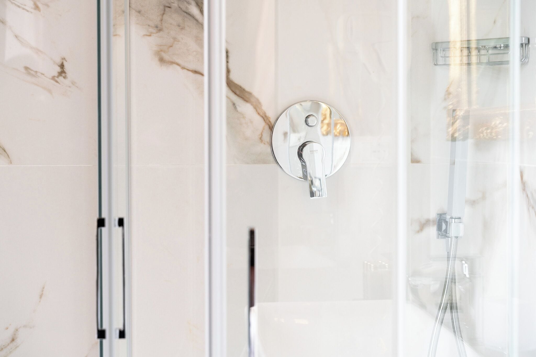 Une salle de bain moderne avec une douche à parois de verre, un mur recouvert de carreaux de marbre et un robinet rond en métal.