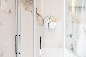 A modern bathroom with a glass shower enclosure, a marble-tiled wall, and a round, metallic faucet.