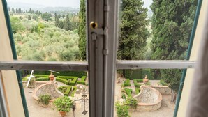 A view through a window of a well-maintained garden with geometric landscaping, stone structures, and potted plants.
