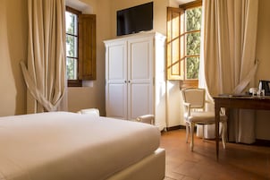 Una camera d'albergo con un letto grande, una scrivania con una sedia, un armadio e un televisore montato a parete.