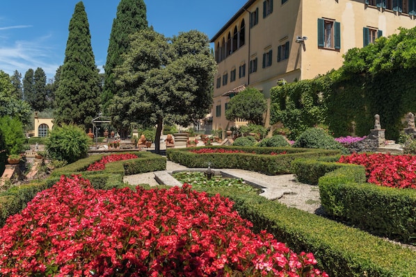 Un jardín formal con setos perfectamente recortados, una fuente y estatuas.