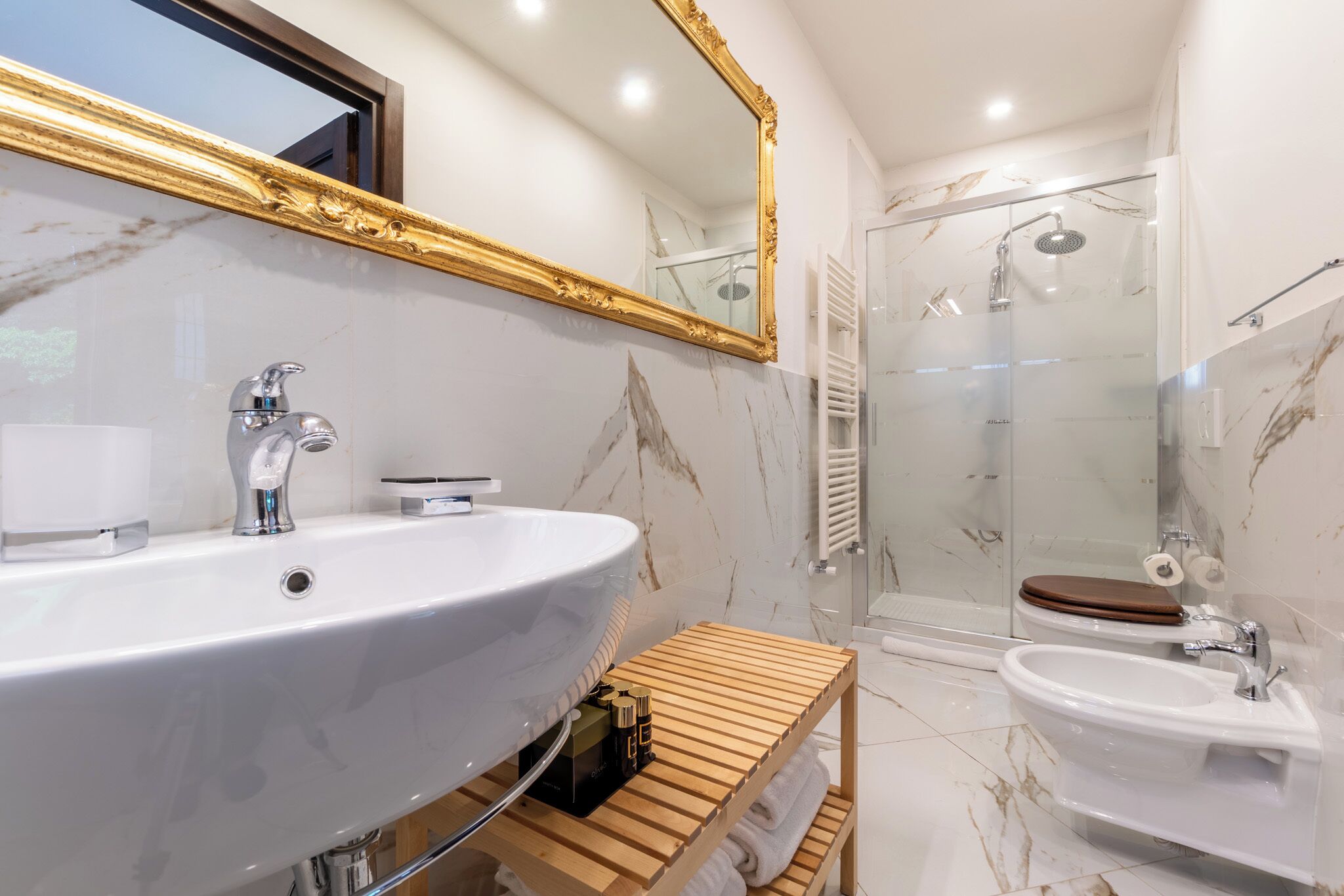 A bathroom with a large white sink, a wooden vanity, a glass shower enclosure, and a white pedestal sink.