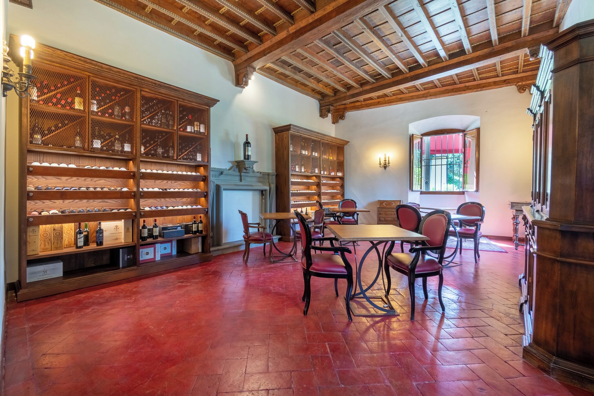 A library with wooden bookshelves and a fireplace, a dining area with red chairs, and a red-tiled floor.