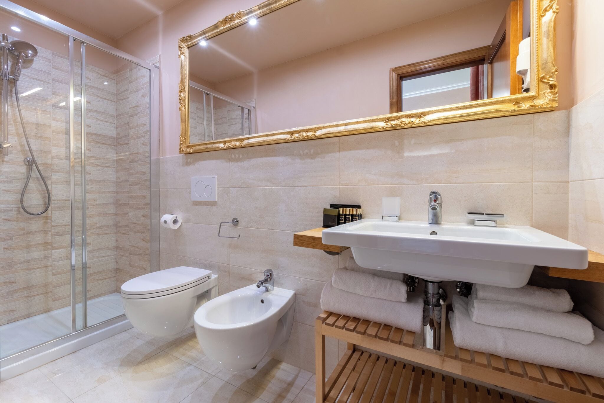 Un baño moderno con cabina de ducha de vidrio, inodoro, bidé, lavabo con tocador y un espejo grande con marco dorado.