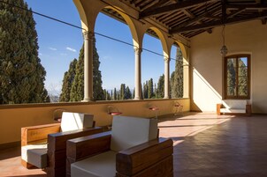Una terrazza aperta con mobili in legno, pavimento piastrellato e vista su alberi alti e una montagna.