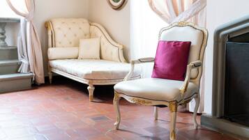 A room with a white sofa, a chair with a pink cushion, and a fireplace.