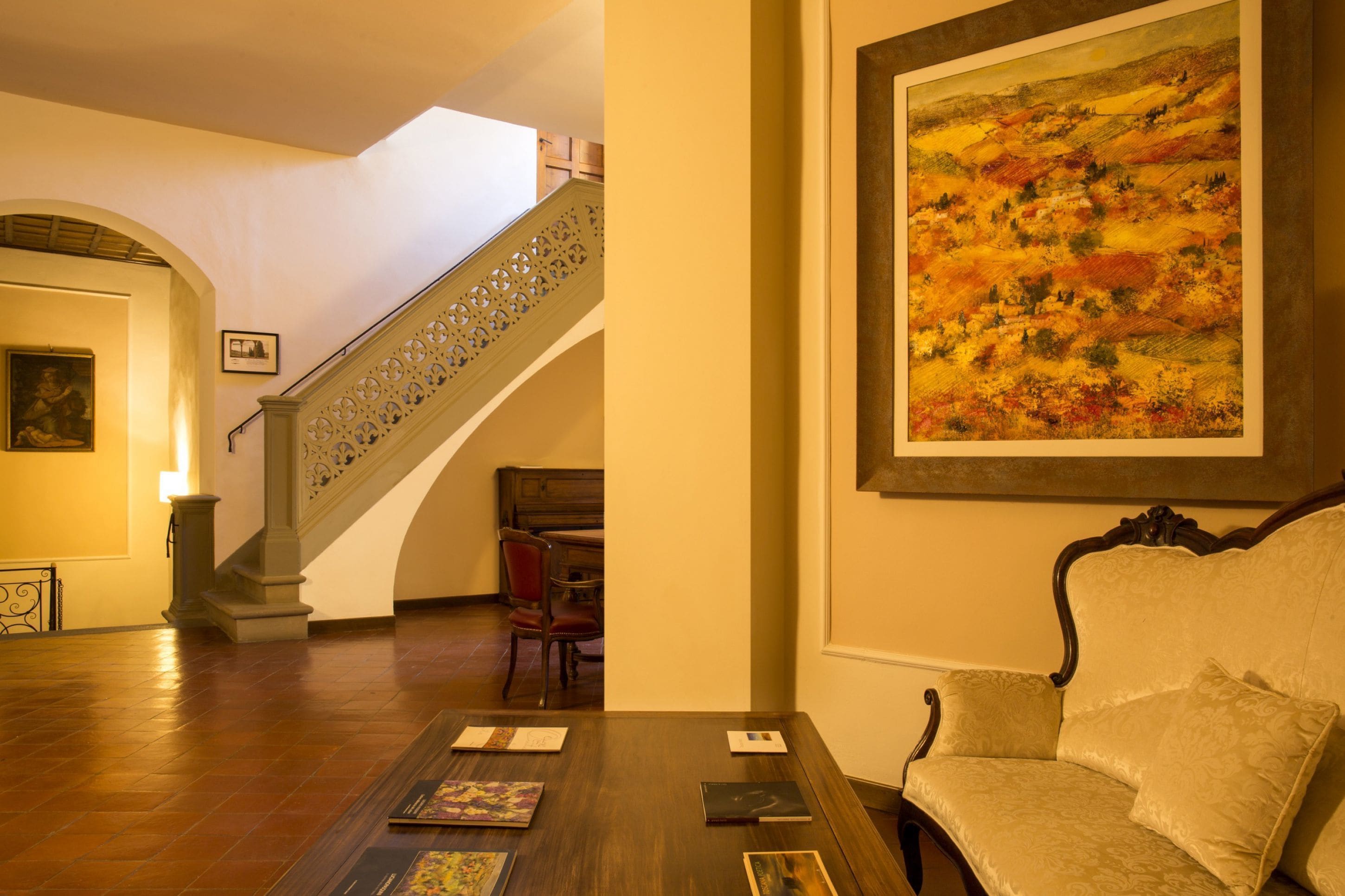 A room with a wooden floor, a sofa, a table with books, a staircase, and a painting on the wall.
