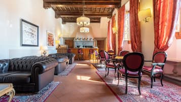 A spacious living room with a black leather sofa, a dining area with red chairs, a bar with a wine display, and a chandelier.