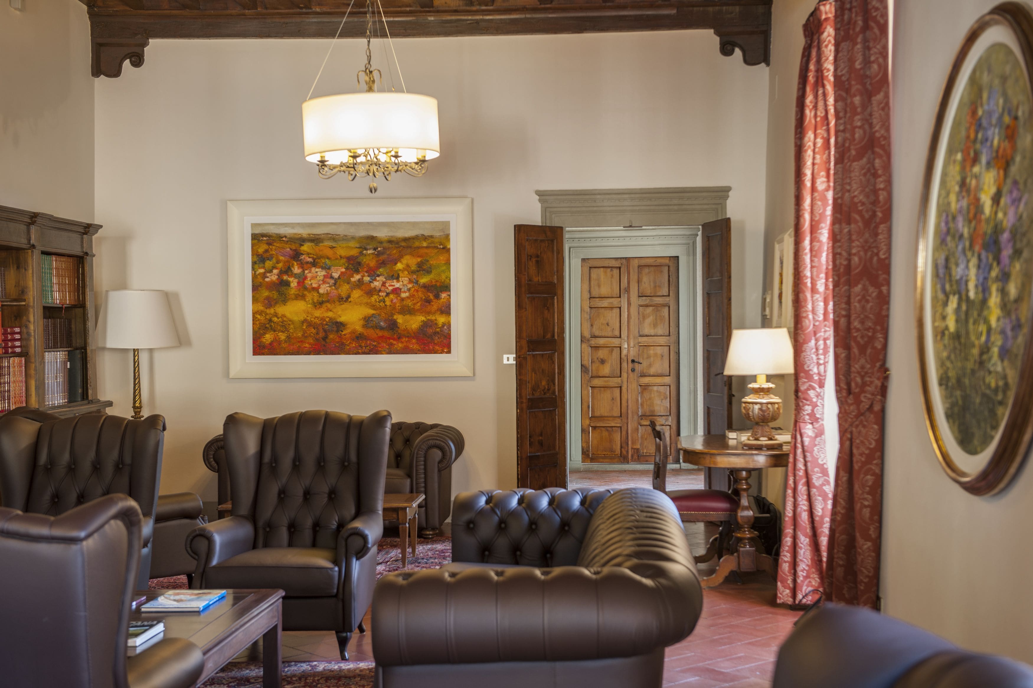 A living room with leather armchairs, a sofa, a chandelier, a painting, a wooden door, and a bookshelf.