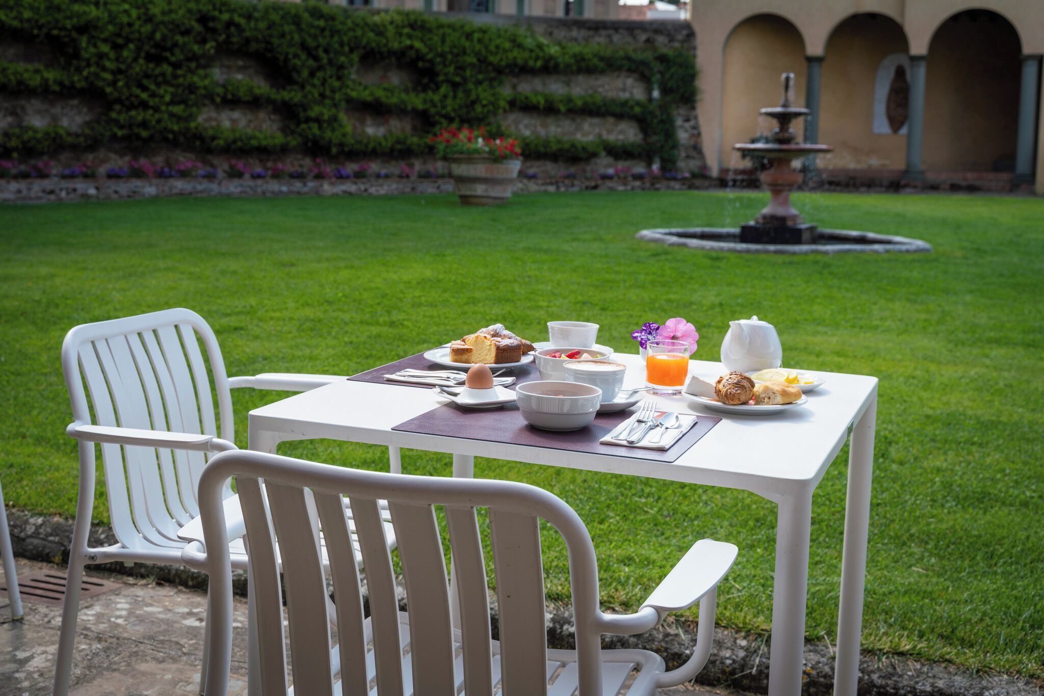 A table set for breakfast with a view of a fountain and greenery in the background.
