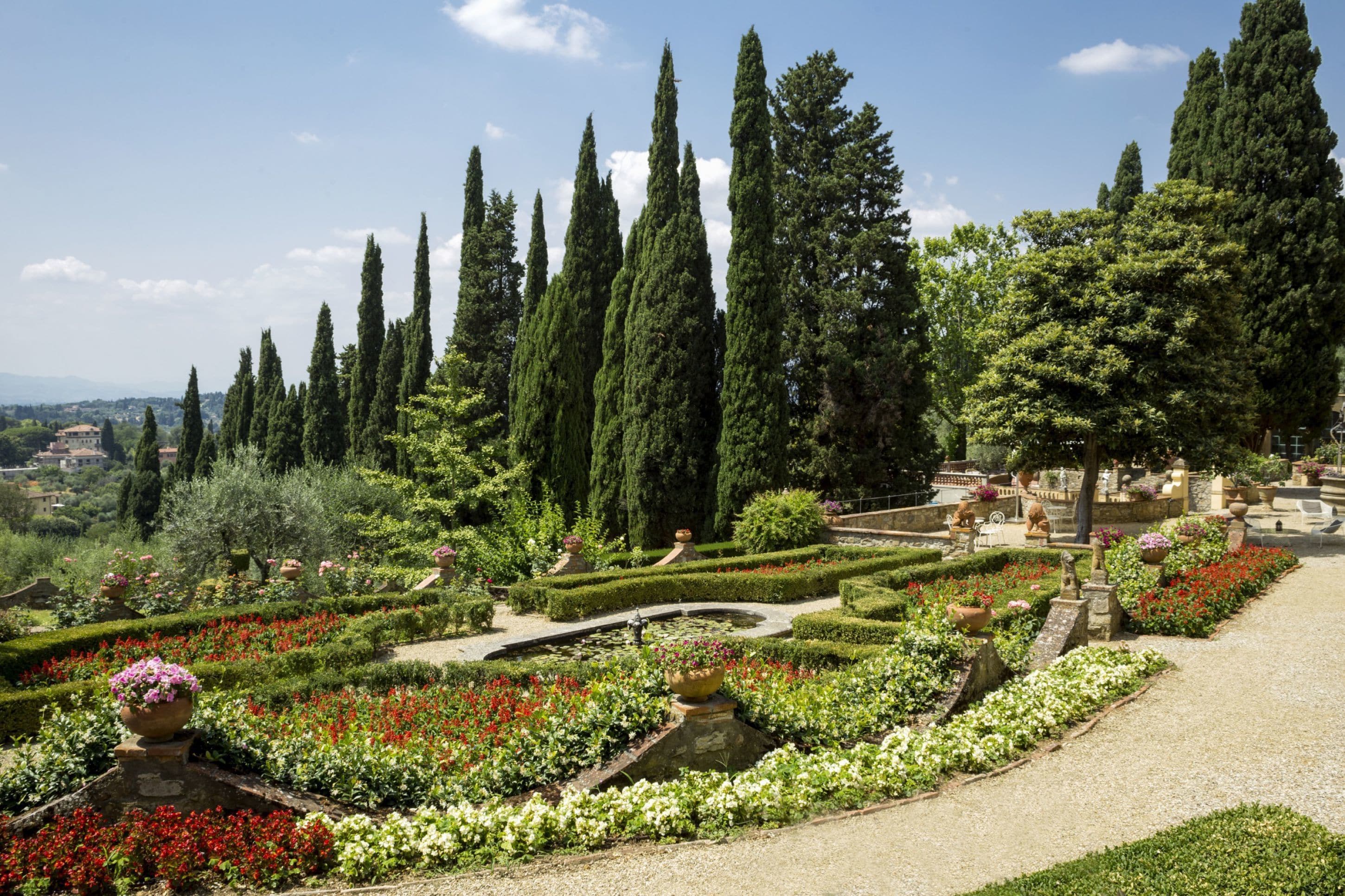 Un jardín formal con setos cuidadosamente recortados, una fuente central y altos cipreses.