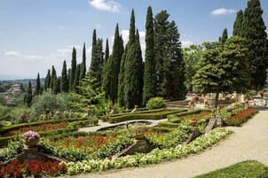Un jardín formal con setos cuidadosamente recortados, una fuente central y altos cipreses.