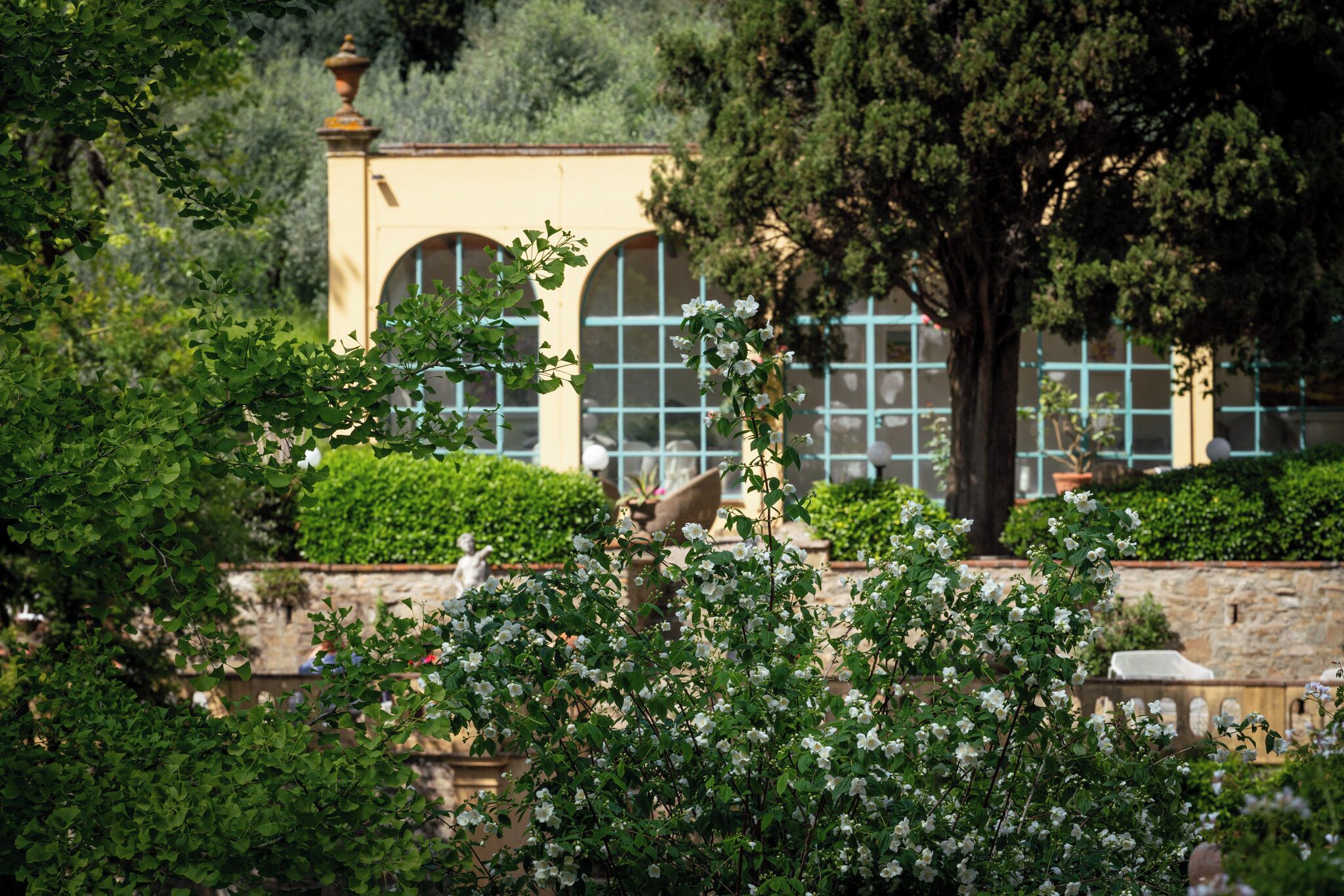 A garden with a fountain, a building with arched windows, and a statue.