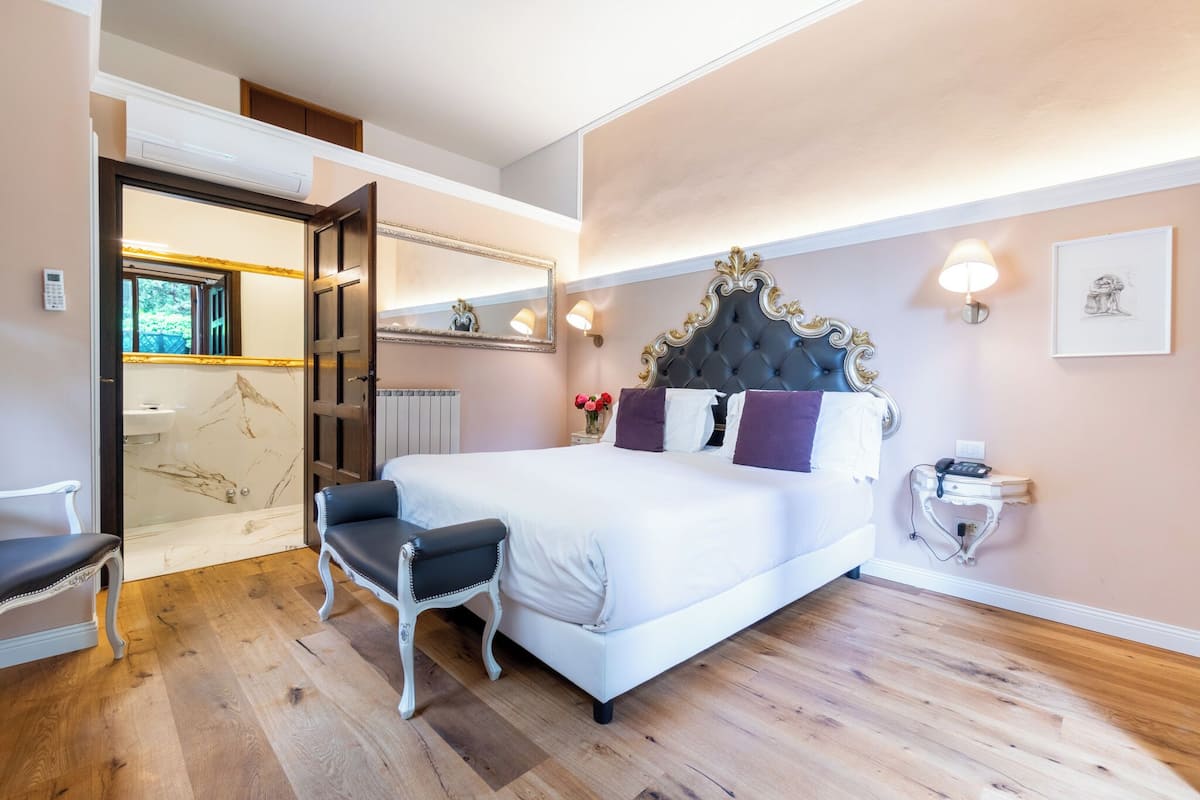 Un dormitorio con una cama grande, una mesita de noche, una silla, un espejo y una ventana.