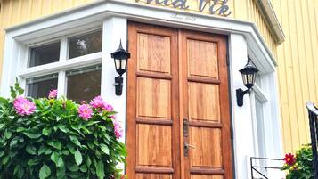 Edifício de esquina com porta dupla de madeira, placa com o nome 'Villa Vik' e um vaso grande com flores.