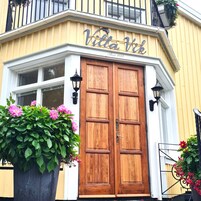 Un edificio en esquina con una puerta doble de madera, un letrero que dice 'Villa Vik' y una maceta grande con flores.