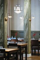 Interior de restaurante con paredes de paneles de mármol, mesas de madera y candelabros colgantes.