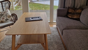 A modern living room with a wooden coffee table, a sofa with cushions, and a view of a lake through large windows. - Toftastrand Hotell (Växjö)