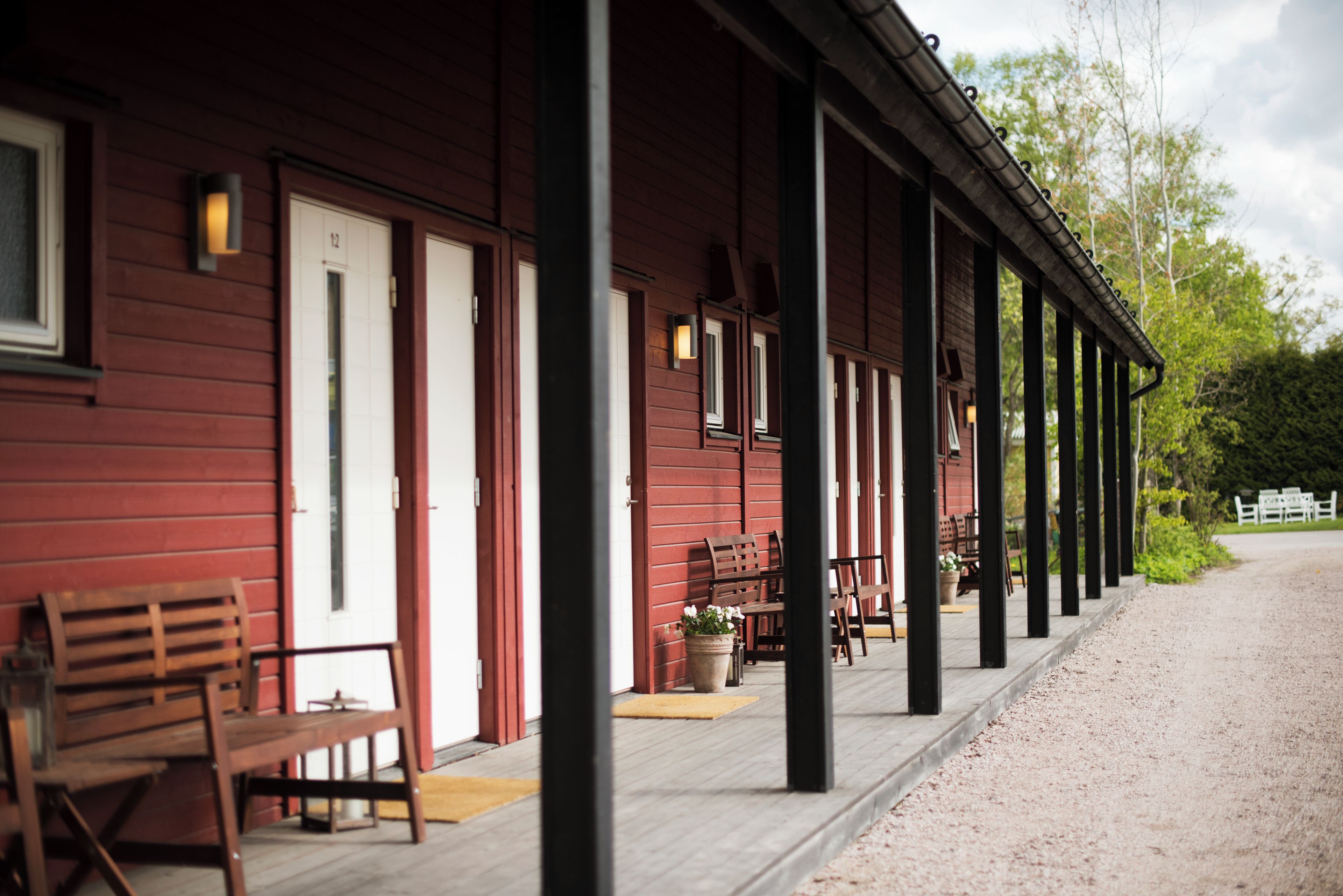 A red wooden building with a covered porch, benches, and potted plants.
