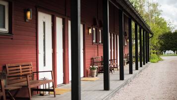 A red wooden building with a covered porch, benches, and potted plants.