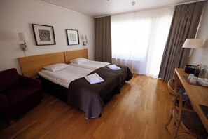 Habitación de hotel con una cama doble, un escritorio con silla, un sillón rojo y una ventana con cortinas.