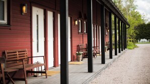 A red wooden building with a covered porch, benches, and potted plants. - Toftastrand Hotell (Växjö)