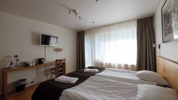 Una habitación de hotel con cama, escritorio, silla, televisor y ventana con cortinas.