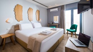 Una moderna camera d'albergo con un letto grande, una scrivania con un portatile, una sedia verde e una TV appesa al muro.