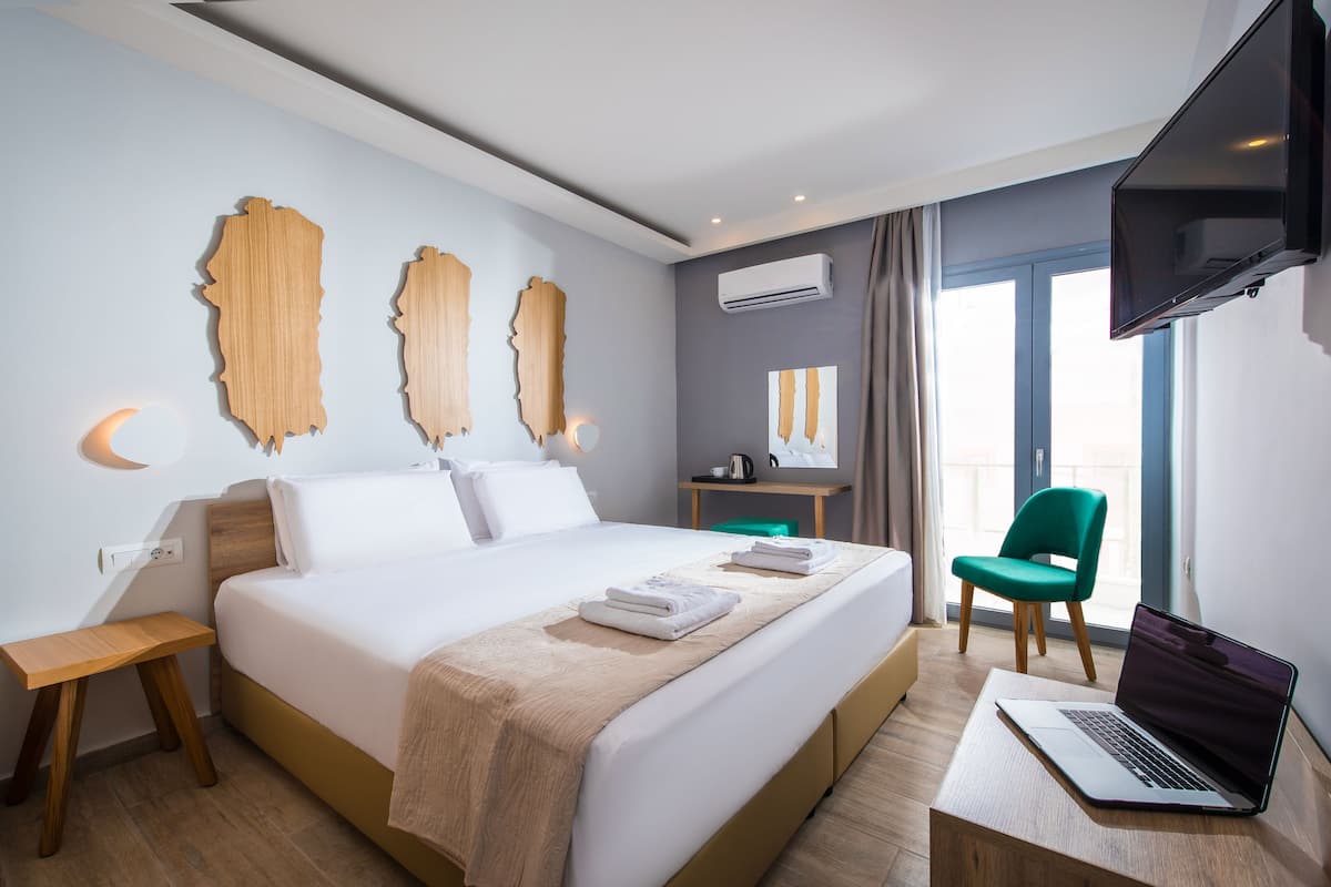 Une chambre d’hôtel moderne avec un grand lit, un bureau avec un ordinateur portable, une chaise verte et un téléviseur fixé au mur.